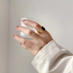 Détail d'une bague chevalière dorée avec onyx noir tenue par une main avec un verre