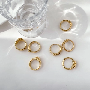 Detailed view of seven gold minimalist rings with twisted and knot designs on a white surface