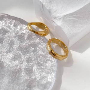 Macro shot of two golden wavy bamboo-style rings on a white stone and glass platform