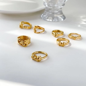 Close-up of golden twist rope rings and knotted stackable bands on a white plate