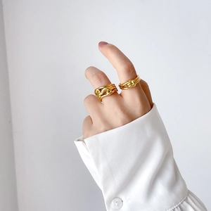Macro view of stacked gold twisted and wave rings on a model's hand in minimalist style