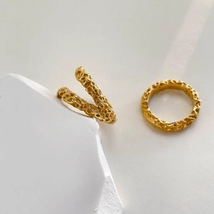 Close-up of dual-layer gold crater rings with irregular hammered texture on stone