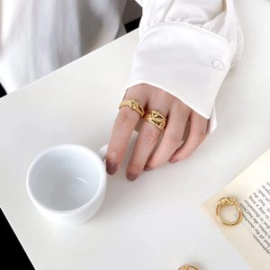 Detail of twisted rope gold rings styled with white shirt and coffee for a chic look