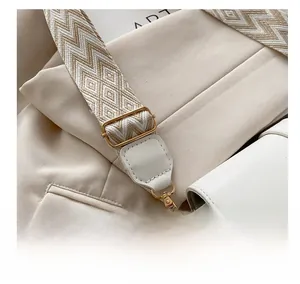 Detail of adjustable geometric woven strap and gold metal buckle on white leather bag