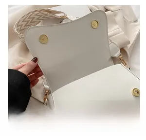 Detail view of white leather saddle bag with gold magnetic snaps and woven strap
