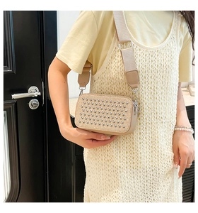 Beige crossbody camera bag with silver rivets and woven strap shown on a model