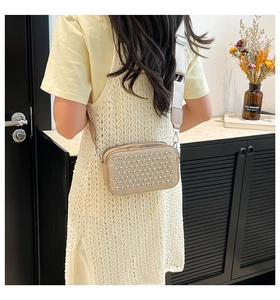 Side view of beige crossbody camera bag with silver studs and wide woven shoulder strap