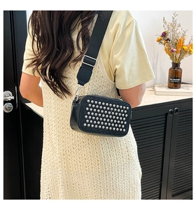 Close-up of trendy black crossbody bag with silver studs and a wide woven shoulder strap