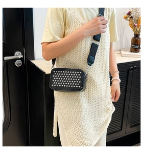Detail of black crossbody bag with silver studs and wide strap on a model