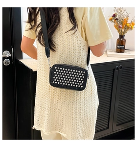 Detail of black glitter crossbody bag featuring silver studs and wide nylon strap