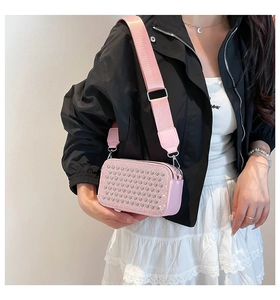 Close-up of pink camera bag with silver studs and a wide fabric shoulder strap