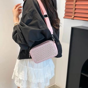 Pink studded crossbody bag with wide fabric strap shown on a model in a stylish interior