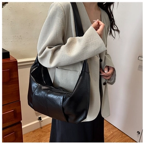 Detail of a large black soft leather dumpling bag showing texture and wide shoulder strap