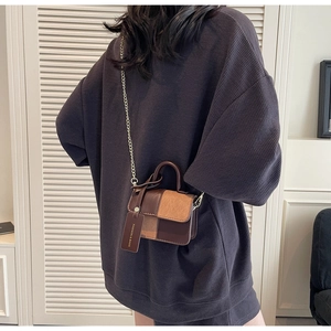Detail of bicolor leather crossbody bag with gold chain strap and decorative tag