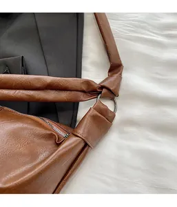 Close-up of silver metal ring buckle and pleated strap on brown leather crossbody bag