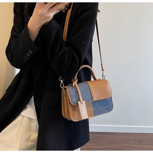 Detail of crossbody bag with brown leather and blue denim patchwork worn by model