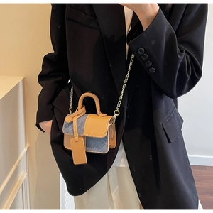 Detail of blue denim and brown leather crossbody bag with a slim gold chain strap
