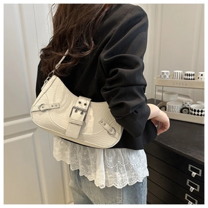Close-up of a white crocodile embossed shoulder bag with silver studs on a female model