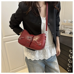 Detail of burgundy crocodile-textured baguette bag with metal buckle and rivets