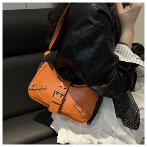 Detail of orange crocodile pattern bag with metallic grommets on a stylish leather outfit