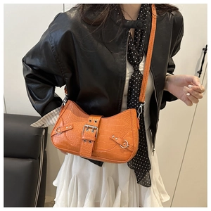 Detail of orange crocodile pattern crossbody bag with silver buckles on a model