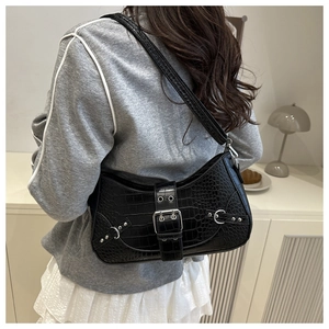 Detail of black faux crocodile baguette bag with silver buckle worn by a model in a room