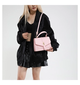 Detailed view of light pink leather crossbody bag with gold buckle on a black jacket