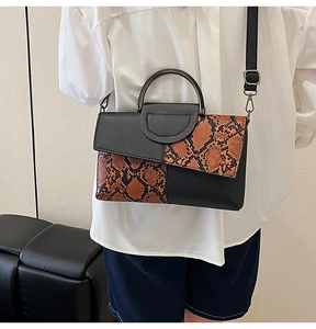 Fashionable snakeskin patchwork handbag worn with shoulder strap and white shirt