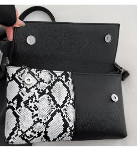 Detail of snake skin pattern flap and metal magnetic closure on black leather crossbody bag