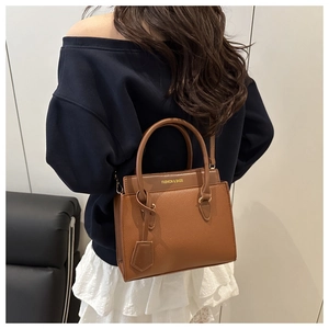 Sac à main marron avec texture litchi et lettrage porté par un mannequin élégant