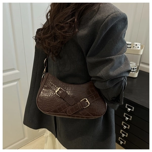 Detail of dark brown crocodile pattern shoulder bag with decorative golden metal buckles