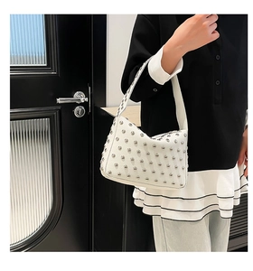Detail of white leather shoulder bag featuring silver rivets and a punk-style curved shape