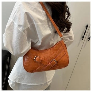 Detail of orange crocodile pattern underarm bag with decorative belt buckle straps