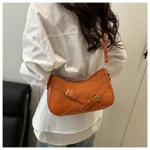 Detail of orange faux leather shoulder bag with crocodile texture and decorative buckles