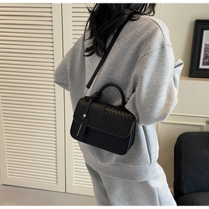 Detail of black crossbody bag featuring woven leather texture and fashion luggage tag