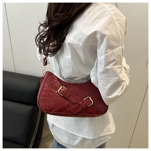 Detail of dark red crocodile pattern shoulder bag with decorative golden buckles