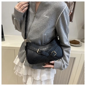 Detail of black faux crocodile skin shoulder bag with double buckle straps on model