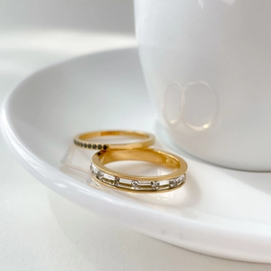 Ensemble de bagues dorées avec pierres noires et zircons sur fond blanc épuré