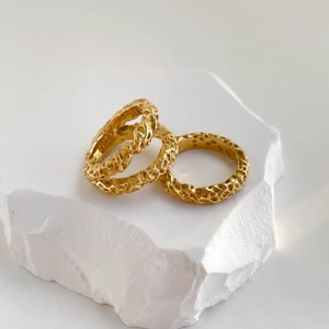 Detail shot of two gold crater texture rings on white stone showing hammer finish pattern