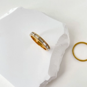Détail d'une bague dorée aux cristaux baguette sur socle en pierre au style épuré