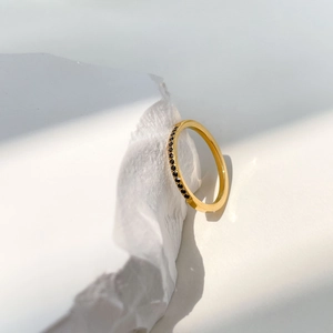 Détail d'une bague dorée minimaliste sertie de pierres noires sur papier froissé