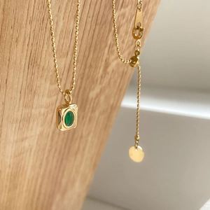 Close-up of gold beaded chain necklace with an emerald pendant on a wooden stand
