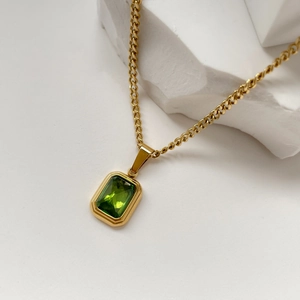 Close-up of emerald pendant necklace with gold chain on white marble background