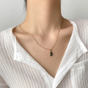 Close-up of elegant gold necklace with deep blue emerald-cut stone on a model