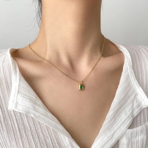 Elegant gold necklace with emerald pendant shown on a model wearing a white shirt