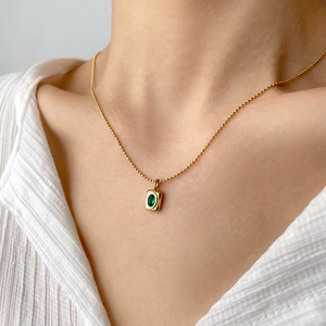 Detail of 18K gold ball chain necklace with rectangular emerald stone pendant on model