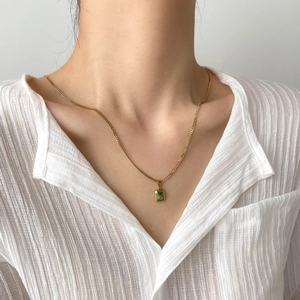 Detail of emerald green pendant necklace on model wearing white translucent shirt