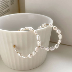 Detailed view of handmade C-shaped earrings with irregular baroque pearls and gold metal