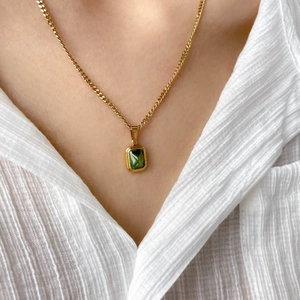 Close-up of a gold chain necklace with a rectangular emerald green pendant on a model