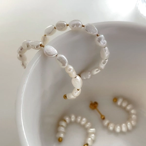 Detailed view of handmade baroque pearl hoop earrings on a minimalist white ceramic bowl